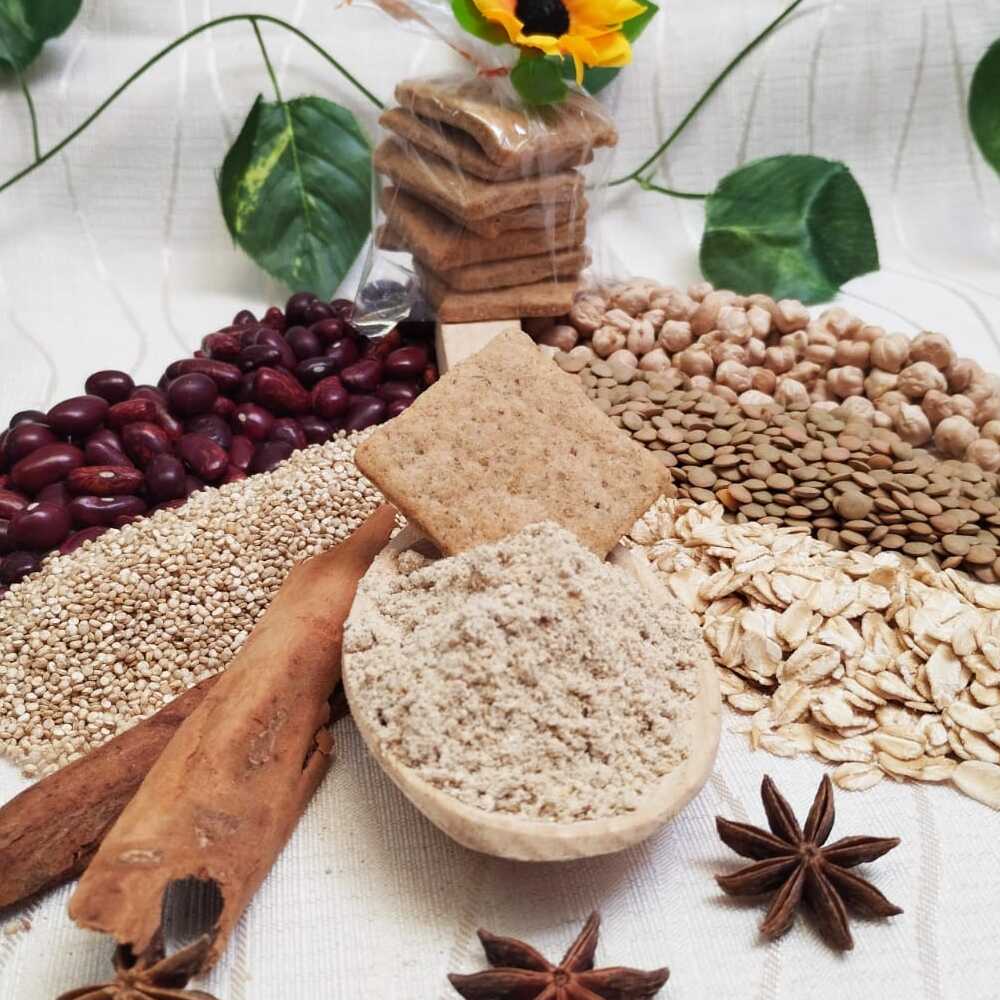 Al centro una galleta de FMix en una cuchara llena de harina precocida FMix. Alrededor, decoración compuesta por los ingredientes de las galletas. Al fondi, un paquete de galletas y decoración de flores.