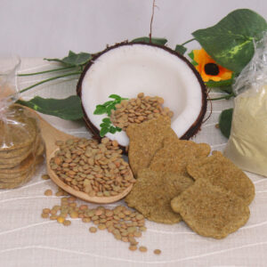Al centro, galletas de lentejas, coco y moringa con forma de osito. Alrededor, decoración compuesta por la mitad de un coco, una cuchara de madera conteniente lentejas enteras, lentejas esparcidas, hojitas de moringa y flores.