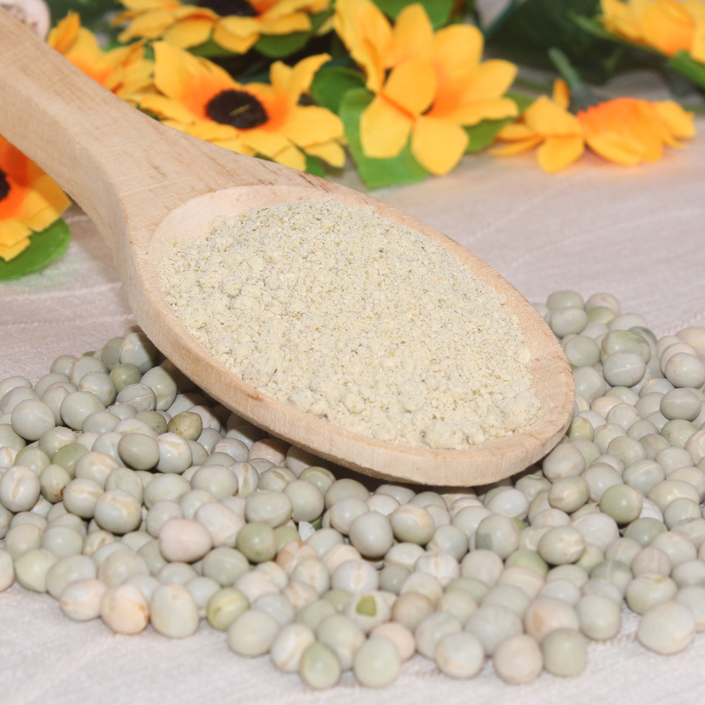 Al centro, cuchara de madera conteniente harina de arvejas precocidas. Decoración compuesta por arvejas enteras, flores amarillas y hojas.