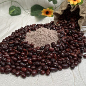 Al centro, montañita de harina precocida de frijoles. alrededor, frijoles enteros esparcidos. Decoración de una bolsa de tela de la cual salen los frijoles, flores amarillas y hojas.