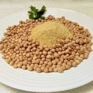 En un plato redondo blanco, al centro una montañita de harina precocida de garbanzos. Alrededor garbanzos enteros esparcidos. Decoración con hojitas verdes.