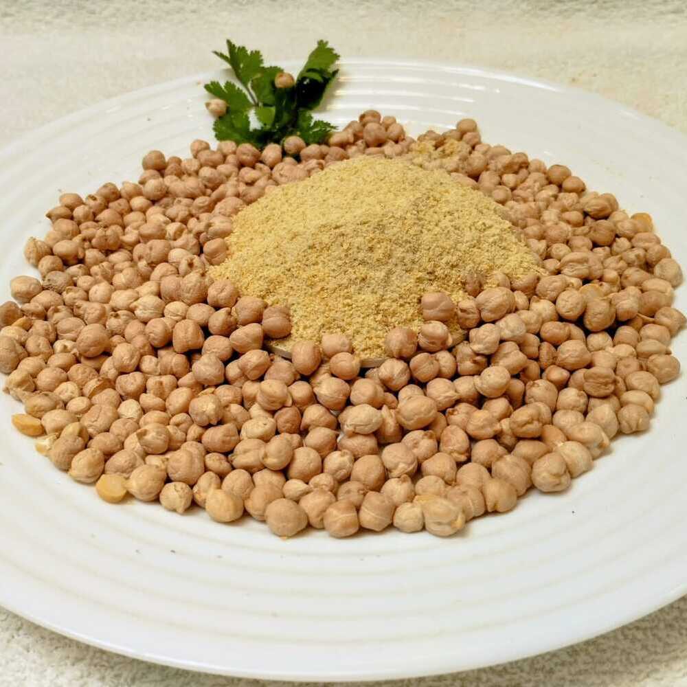 En un plato redondo blanco, al centro una montañita de harina precocida de garbanzos. Alrededor garbanzos enteros esparcidos. Decoración con hojitas verdes.
