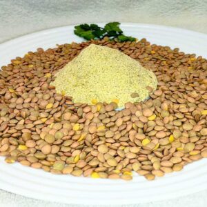 al centro, un mucchietto di farina precotta di lenticchie. la circondano delle lenticchie intere. sullo sfondo, decorazione di foglioline verdi.