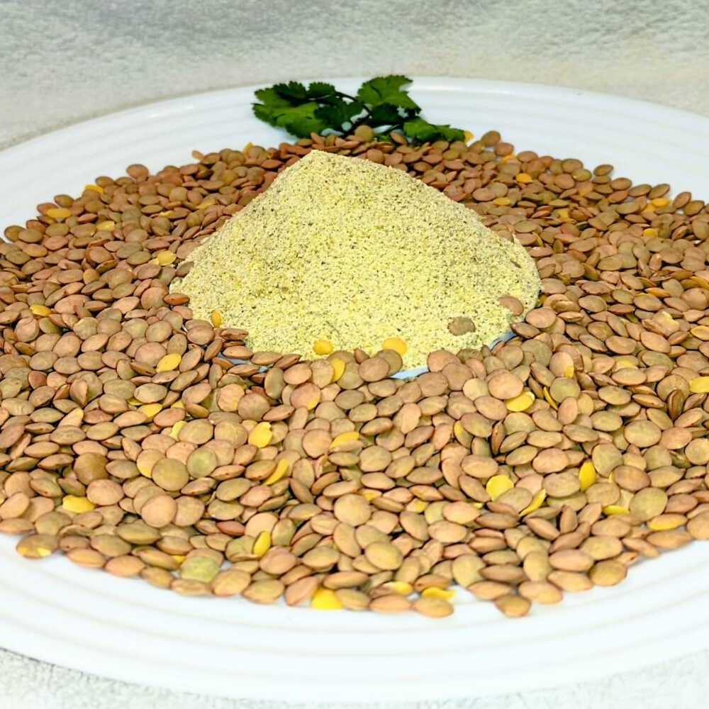 Al centro, montañita de harina precocida de lentejas. Alrededor, lentejas enteras esparcidas. Decoración con pequeñas hojas verdes.